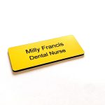 A Yellow name badge with black engraved text. With rounded corners