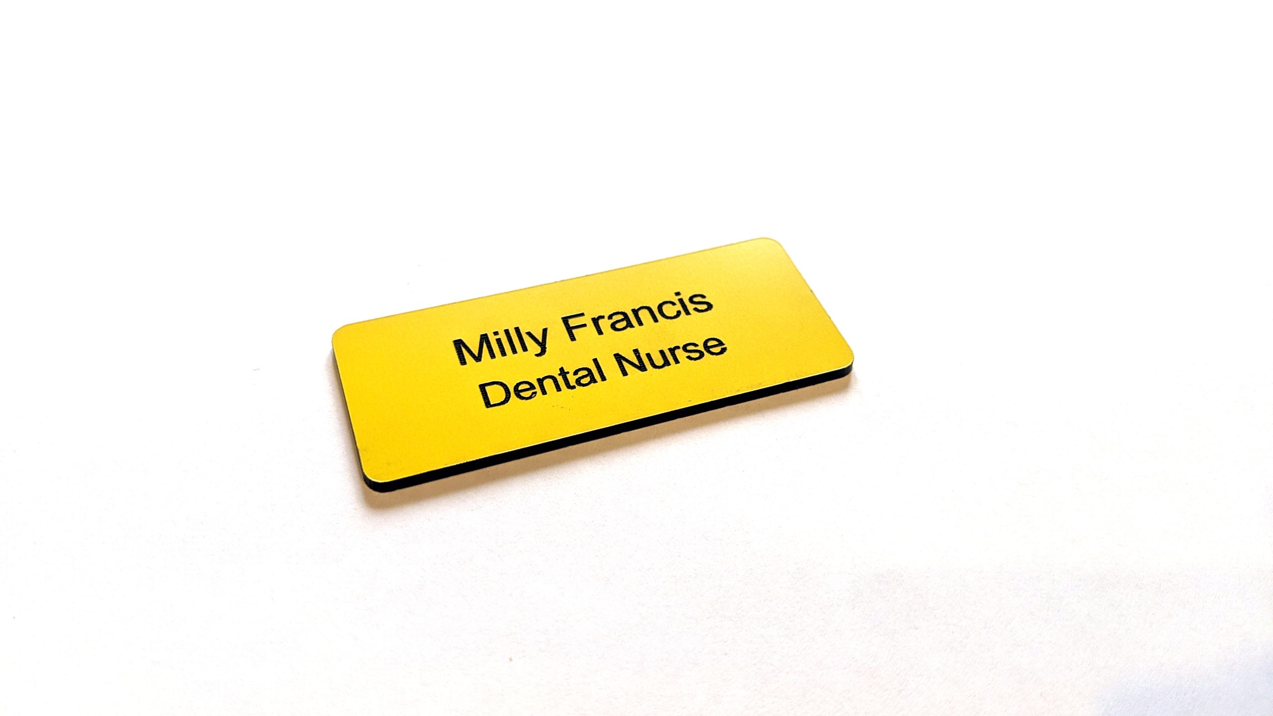 A Yellow name badge with black engraved text. With rounded corners