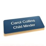 A navy blue name badge with white engraved text. With rounded corners