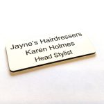 A white name badge with black engraved text. With rounded corners