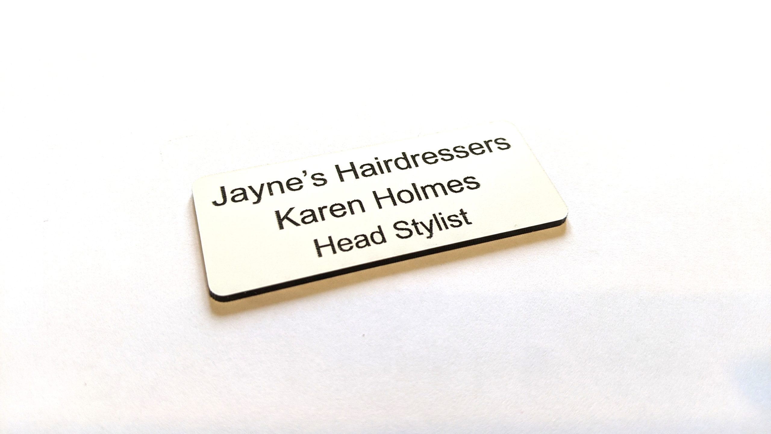 A white name badge with black engraved text. With rounded corners
