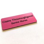 A pink name badge with black engraved text. With rounded corners