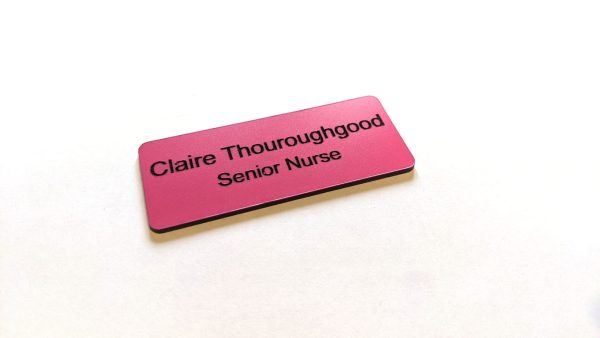 A pink name badge with black engraved text. With rounded corners