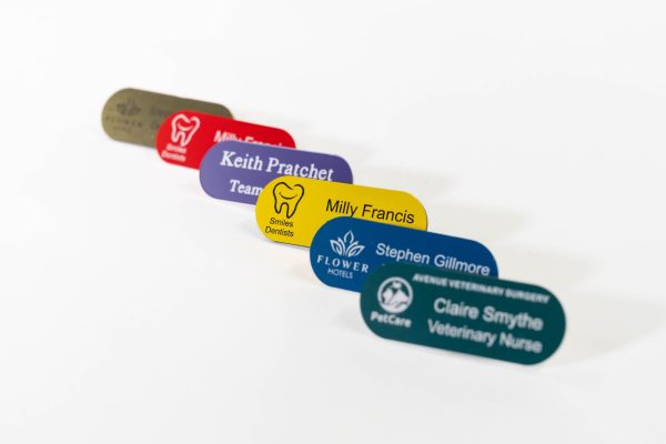 Various pill shaped engraved name badges with and without logos on the left.