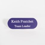 A pill shaped purple badge with white engraved text with oval corners.