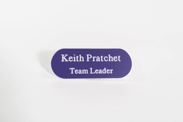 A pill shaped purple badge with white engraved text with oval corners.
