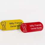 A red pill shaped name badge with white engraved text also a yellow pill shaped badge with black text and smiles dental logo on the left