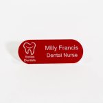 A pill shaped red name badge with white engraved text and smiles dental logo on the left