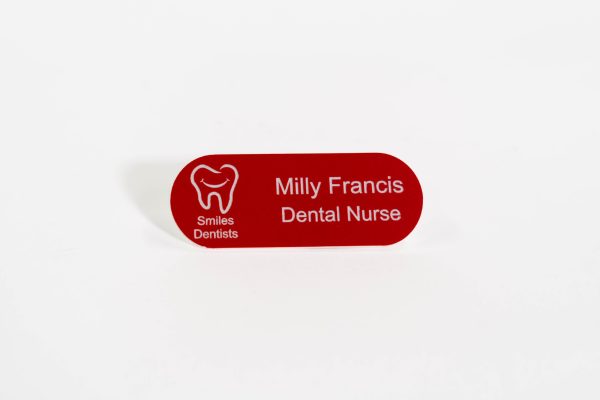 A pill shaped red name badge with white engraved text and smiles dental logo on the left