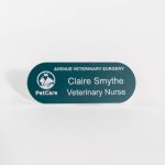 A pill shaped teal green name badge with white engraved text with petcare logo on the left-hand side.