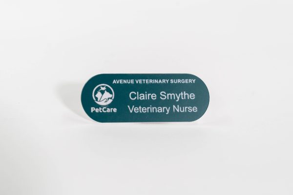 A pill shaped teal green name badge with white engraved text with petcare logo on the left-hand side.