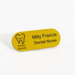 A pill shaped yellow badge with engraved black text and smiles dental logo on the left.