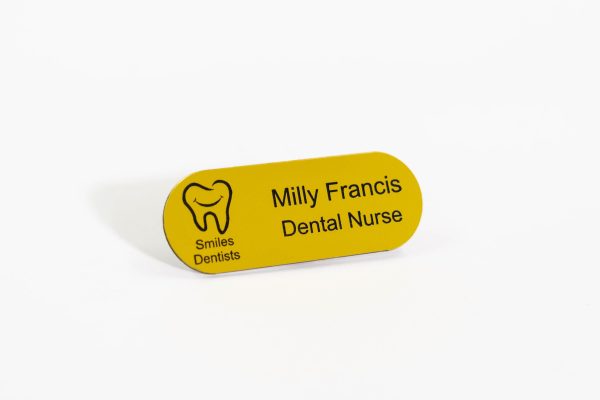 A pill shaped yellow badge with engraved black text and smiles dental logo on the left.