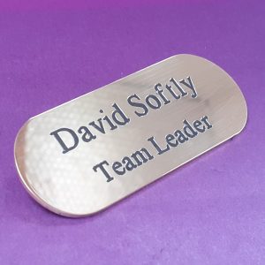A polished brass badge with a pill-like shape, featuring engraved text