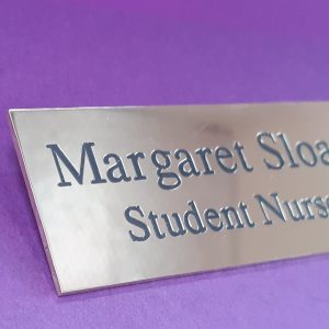 A polished rectangle brass name badge, featuring engraved text