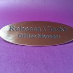 A polished brass badge in the shape of an oval, featuring black engraved text