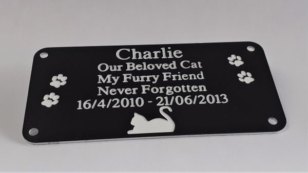 Black rectangle plaque with white engraving text and rounded corners and four screw holes with a cat laying at the bottom and two paw prints either side of the text
