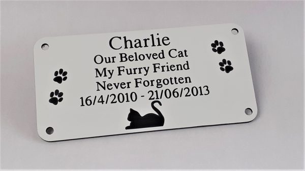 White rectangle plaque with black engraving text and rounded corners and four screw holes with a cat laying at the bottom and two paw prints either side of the text