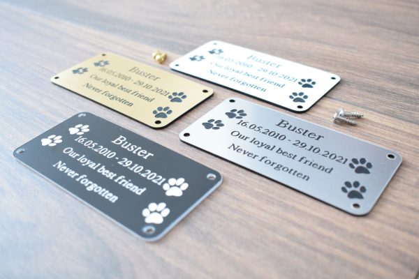 4" x 2 pet memorial plaque, Black rectangle plaque with white engraving text and rounded corners and four screw holes with two paw prints either side of the text