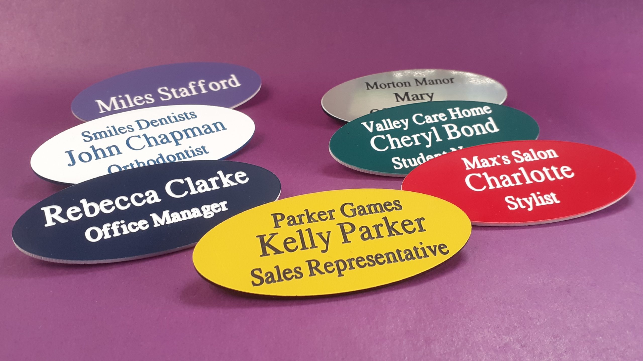 Various coloured engraved oval name badges, engraved with contrasting text.