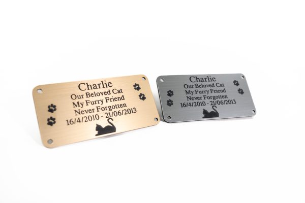 Silver and gold rectangle plaques with black engraving and rounded corners and four screw holes with a cat laying at the bottom and two paw prints either side of the text