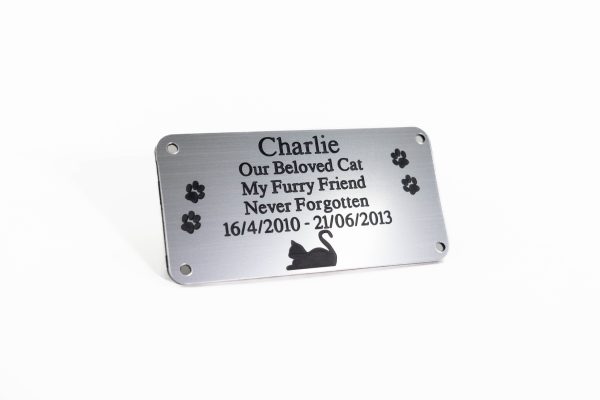 Brushed silver rectangle plaque with black engraving and rounded corners and four screw holes with a cat laying at the bottom and two paw prints either side of the text