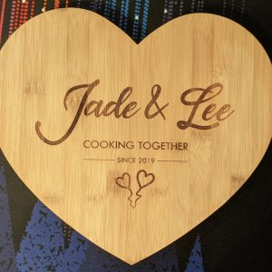 Bamboo heart-shaped chopping board with custom engraving: 'Jade & Lee Cooking Together Since 2019' and two love hearts.