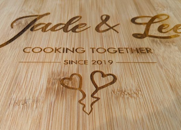 Close up of a heart-shaped bamboo chopping board with heartfelt engraving - 'Jade & Lee - 2019' and two sweet love hearts