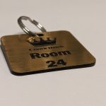 Brushed gold keyring with black text showing a crown logo and a door number