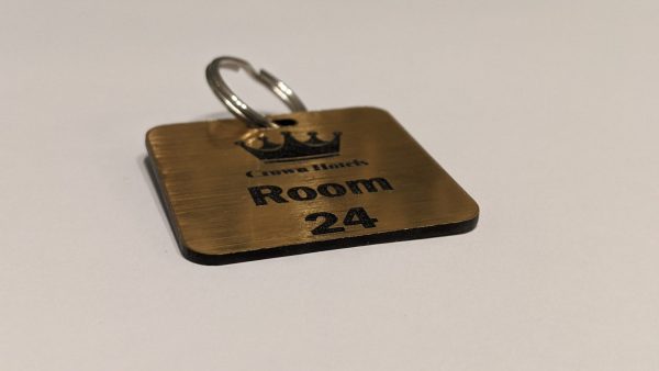 Brushed gold keyring with black text showing a crown logo and a door number