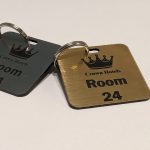 Brushed silver and brushed gold keyring with black text showing a crown logo and a door number