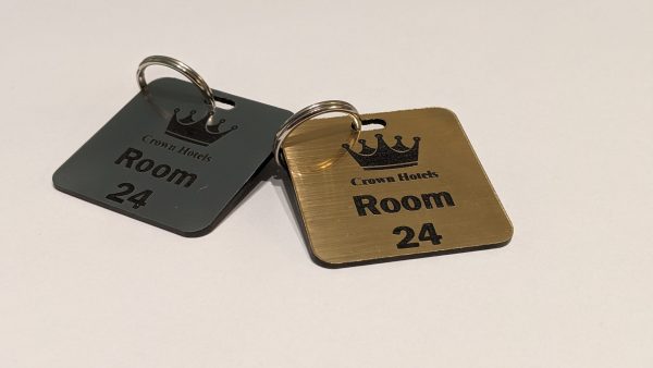 Brushed silver and brushed gold keyring with black text showing a crown logo and a door number