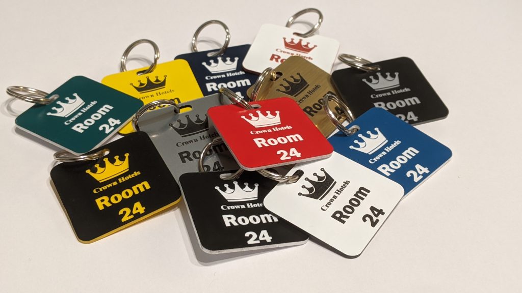 Custom-Engraved Keyrings and Keyfobs showing a crown logo and a door number on in contrasting colours