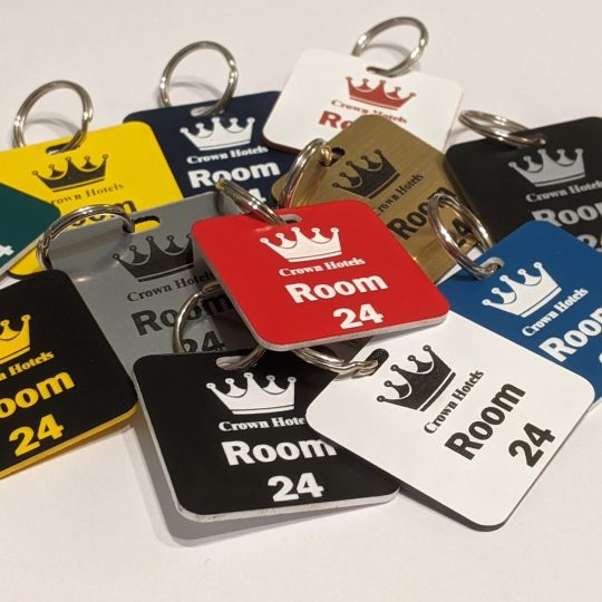 Custom-Engraved Keyrings and Keyfobs showing a crown logo and a door number on in contrasting colours