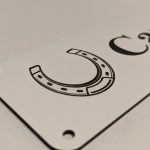 Close up of black engraving on white Stable Name Plaque - 6" x 2" with Left-Hand Horseshoe Design