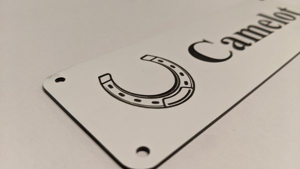 Close up of black engraving on white Stable Name Plaque - 6" x 2" with Left-Hand Horseshoe Design