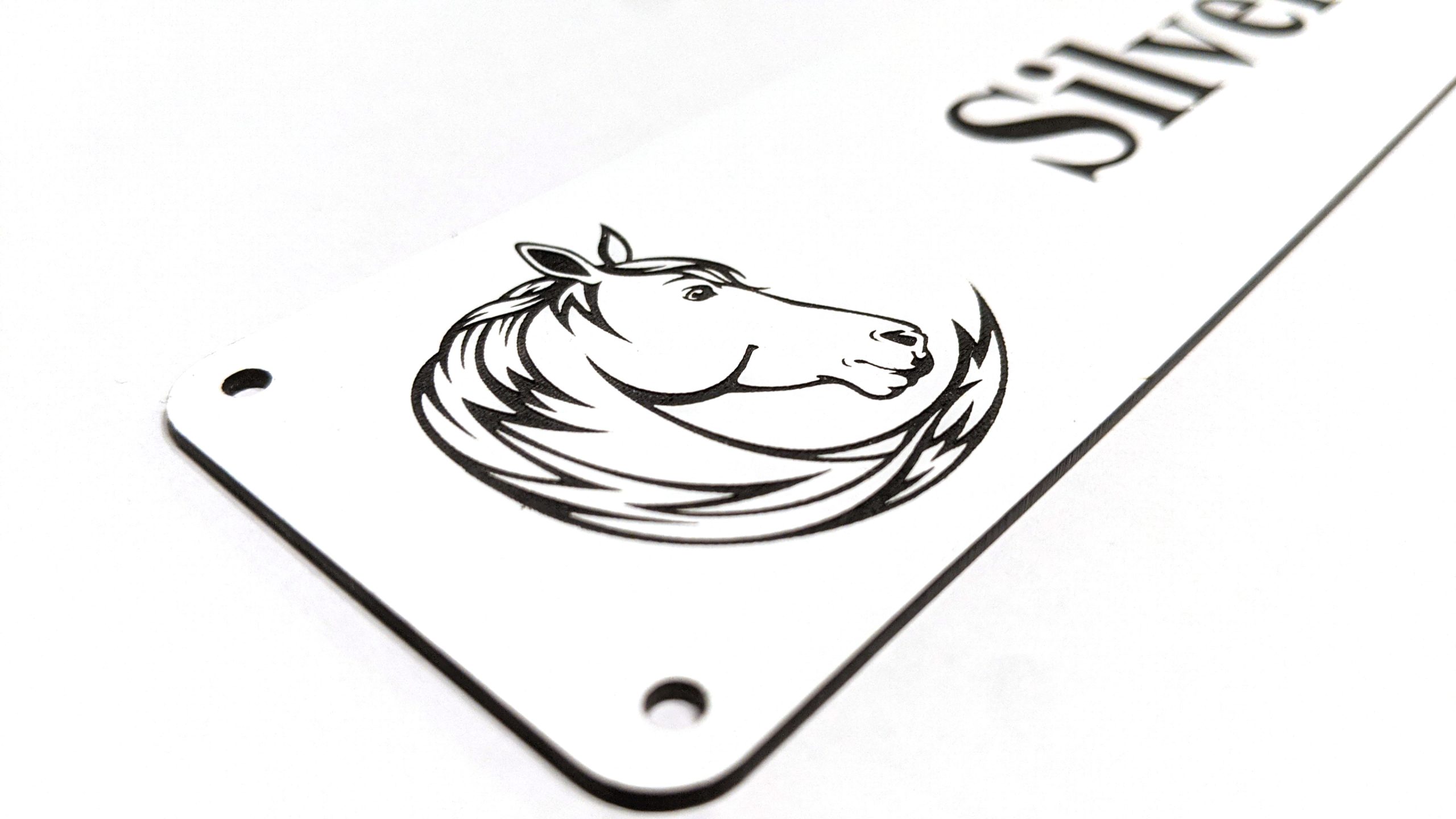 Close up of black engraving on white Stable Name Plaque – 6″ x 2″ with Left-Hand Horse’s Head Design