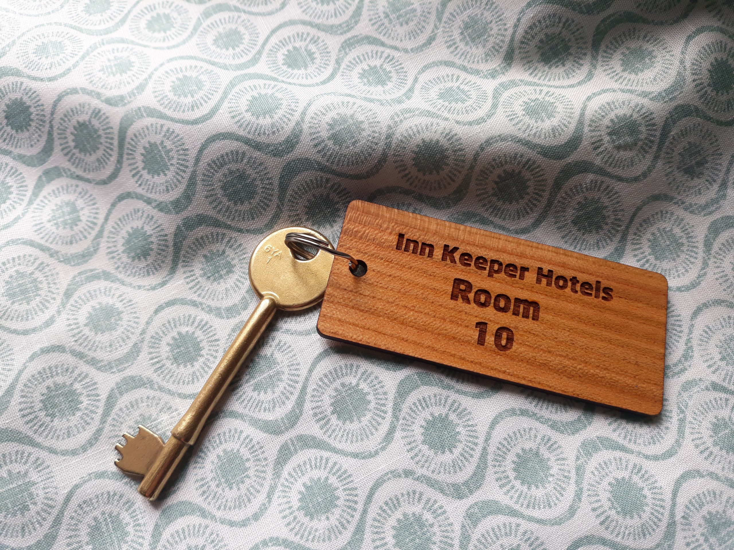 Compact wooden rectangle keyring with a key attached to the split ring featuring detailed engraving showing "Inn Keeper Hotels Room 10"