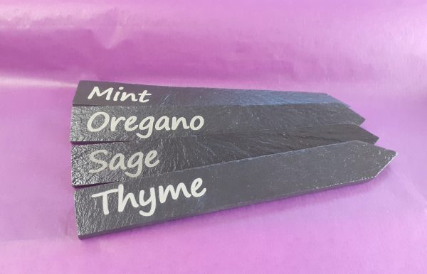 Four sleek, personalised slate plant markers with custom engravings showing Mint, Oregano, Sage, Thyme, adding a touch of modern elegance to your garden or home.