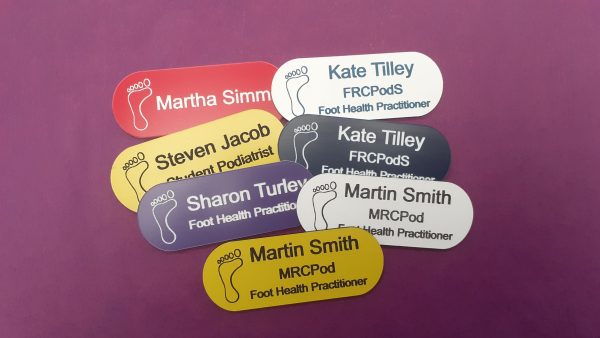 Multicoloured name badges in the shape of a pill with a simple art logo and employee name and title engraved in white or black