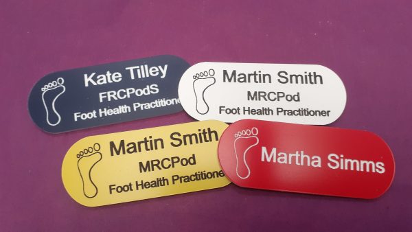 Red, yellow, White, navy blue name badge in the shape of a pill with foot logo and employee name and title engraved in black or white text