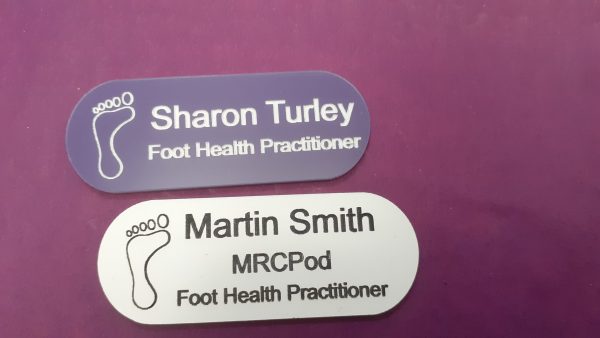 Purple and white name badge in the shape of a pill with foot logo and employee name and title engraved in black or white text