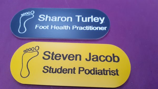 Blue and Yellow name badge in the shape of a pill with foot logo and employee name and title engraved in black or white text