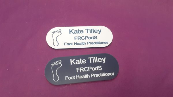 White, Black name badge in the shape of a pill with foot logo and employee name and title engraved in black or white text