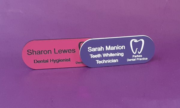 Purple and pink name badge in the shape of a pill with a tooth logo and employee name and title engraved in black or white text