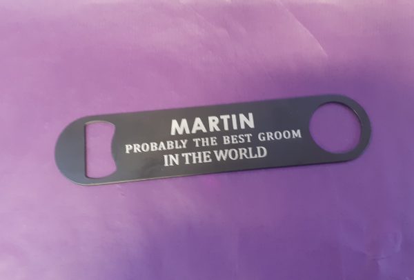 Stainless steel Bar Blade Bottle Opener with laser engraved text, showing the best groom and a person name