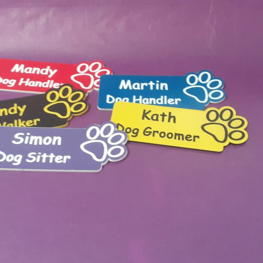 A collection of vibrant and diverse name badges, each uniquely coloured in shades such as blue, red, green, and yellow. The badges are designed with a paw print on the right-hand side of the badge.