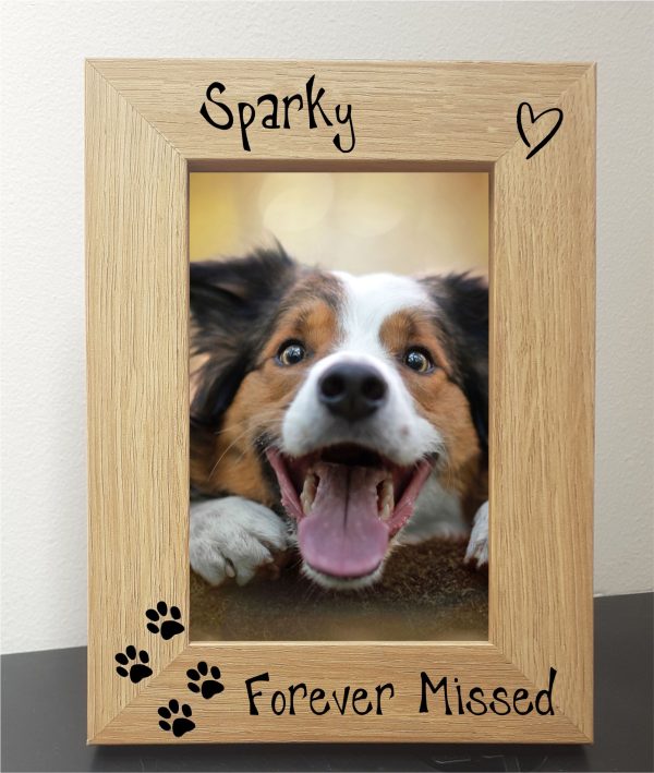 An oak veneer photograph frame. It has been personalised with text etched on the frame, with the dog’s name at the top of the frame, forever missed at the bottom, 4 paw prints etched in the bottom left-hand side of the frame, a heart top right