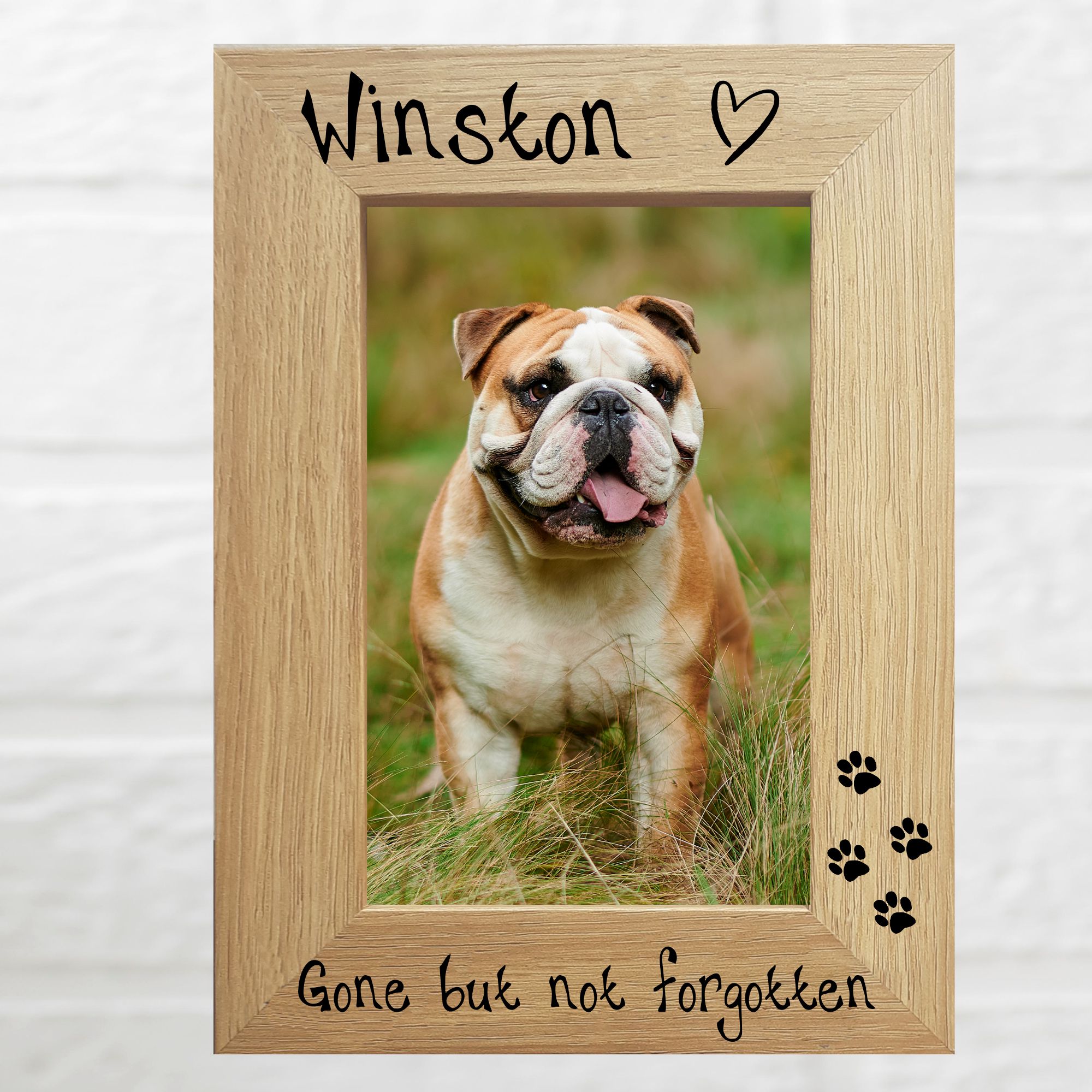 An oak veneer photograph frame. It has been personalised, with the dog’s name at the top of the frame, gone but not forgotten at the bottom, 4 paw prints etched in the right-hand side of the frame, a heart etched top