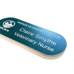 Teal Green with white text in the shape of a pill name badges, Logo to the left-hand side of the badge displaying Petcare. The top line says Avenue Veterinary Surgery underneath a new line saying Claire Smythe and the 3rd line says Veterinary Nurse. The badge is on a clean white background